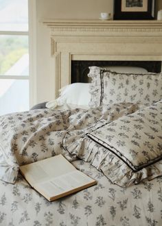 an open book sitting on top of a bed in front of a fire place next to a window