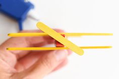 a hand holding two yellow toothpicks in front of a blue and white object