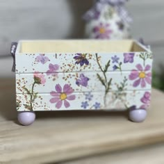 a small wooden box with flowers painted on the sides and wheels, sitting on top of a table