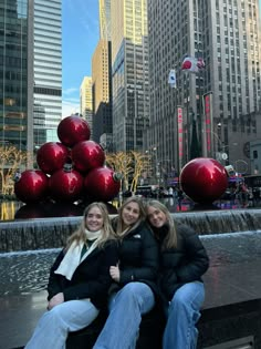 two women sitting on the edge of a fountain with christmas balls in the air behind them