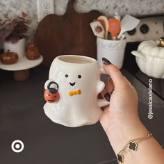 a hand holding a coffee mug with a ghost face on it and pumpkins in the background