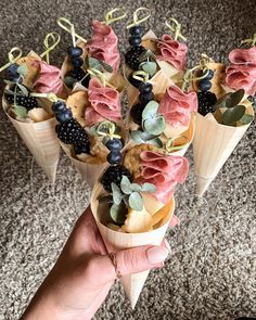 a person holding some cones filled with fruit and veggies on top of carpet