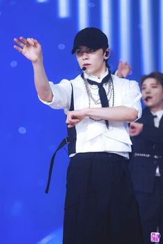 a male in a white shirt and black tie standing on stage with his hands up