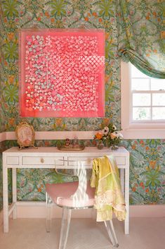 a white desk sitting under a window next to a wall covered in pink and green flowers