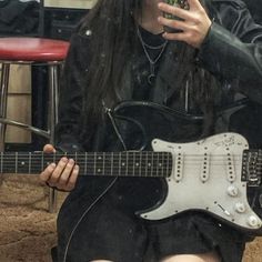 a woman with long black hair is holding a guitar and looking at her cell phone