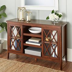 a wooden sideboard with books and vases on the top, in front of a mirror