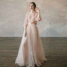 a woman in a pink dress standing on a wooden floor with her hands behind her head