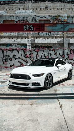 a white sports car parked in front of a graffiti covered wall with writing on it