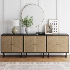 a sideboard with two vases and a round mirror on it next to a lamp