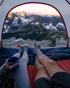 a person laying in a tent with their feet up on the ground and mountains in the background