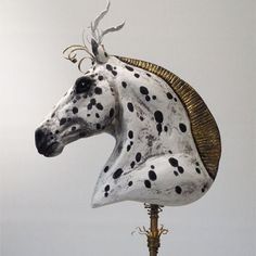 a white and black spotted horse head sitting on top of a metal stand with gold accents