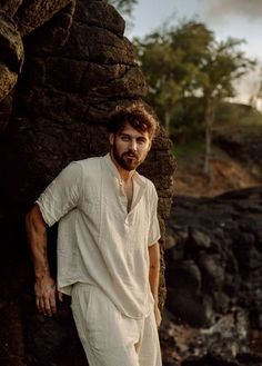 a man leaning against a large rock near the ocean with his hands on his hips