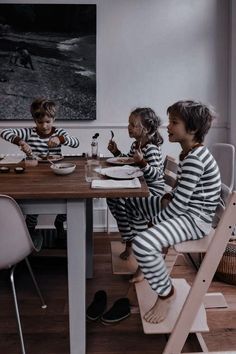 three children sitting at a table with food in front of them and one child standing up