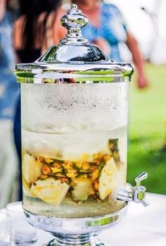 a glass jar filled with ice and fruit on top of a table next to people