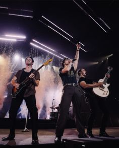 the band is performing on stage with their guitars up in the air as fireworks go off behind them