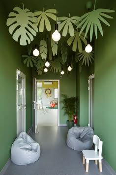 a room with green walls and white chairs on the floor in front of it is an indoor area that has large palm leaves hanging from the ceiling