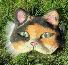 a cat mask laying in the grass with eyes wide open and one eye half closed