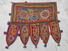 an embroidered wall hanging with tassels and beads on the edges, in bright colors