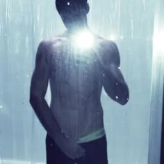 a man standing in front of a shower with the light shining through his shirtless body