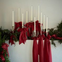 a bunch of candles that are sitting on a mantle with red bows and greenery