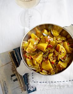 a pan filled with cooked food on top of a white cloth next to silver spoons