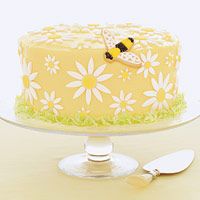 a yellow cake with white daisies and a bee on top is sitting on a table