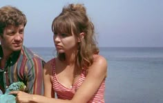 a man and woman standing next to each other near the ocean