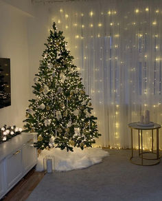 a christmas tree is lit up in the corner of a living room with lights all around it