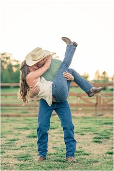 a man holding a woman in his arms while standing on top of a grass covered field