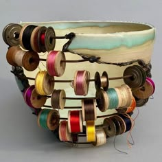 several spools of thread are attached to a white bowl with many different colored spools on it