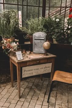 a desk with flowers and an old radio on it in front of a window filled with potted plants