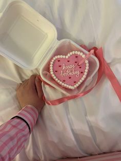 a person is holding a heart shaped cake in a plastic container on a white bed