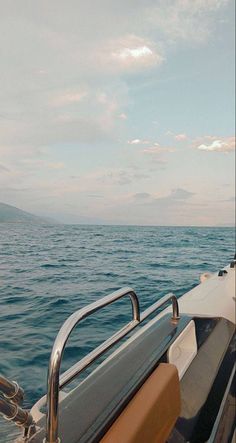 the back end of a boat in the middle of the ocean with mountains in the distance