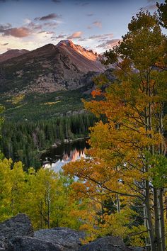 the sun is setting over a mountain range with trees and rocks in front of it