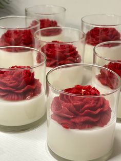 four glasses filled with white and red flowers on top of a table next to each other