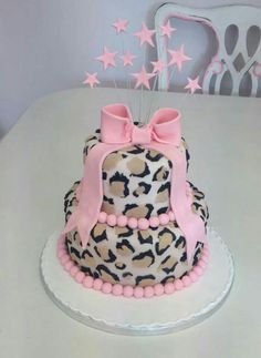 a leopard print cake with pink bows and beads on top, sitting on a white table