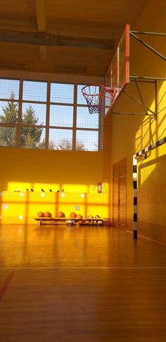 an indoor basketball court with yellow walls and wood flooring is lit by sunlight coming through the windows