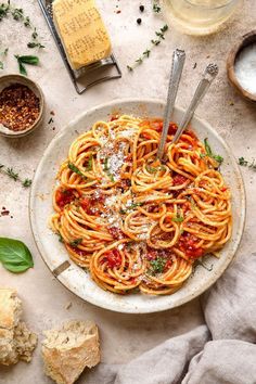 a plate of spaghetti with sauce and parmesan cheese on the side next to breadcrumbs