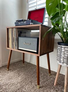 a record player sitting on top of a wooden stand next to a potted plant