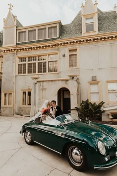 a bride and groom in an old green convertible parked in front of a large building