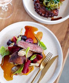 two white plates with food on them sitting on a wooden table next to wine glasses