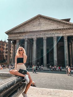 a woman sitting on the edge of a fountain in front of a building with columns