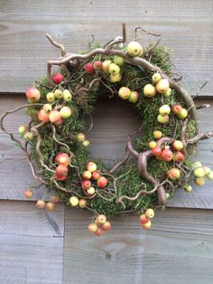 an apple wreath hanging on the side of a wooden fence with apples and grass around it