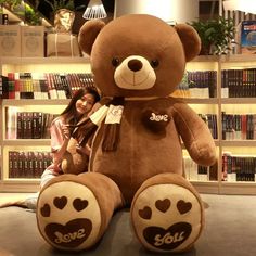 a woman sitting next to a giant teddy bear in front of a book shelf filled with books