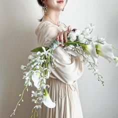 a woman in a white dress holding flowers and looking up at the sky with her eyes closed