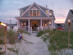 a house on the beach is lit up at night with lights in the windows and grass growing all around