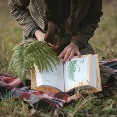 a woman sitting on the ground holding an open book with a fern plant in it