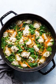 a pot filled with dumplings and vegetables on top of a table next to a towel