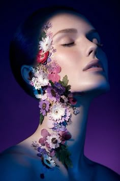 a woman with flowers on her face and neck is shown in the dark blue background