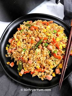 a black plate topped with rice and vegetables next to chopsticks